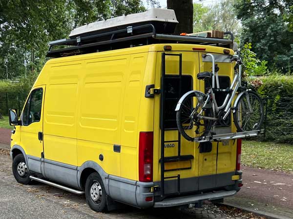 camper met fietsenrek, vaste ladder naar dak, imperiaal met spullen en dakkoffer
