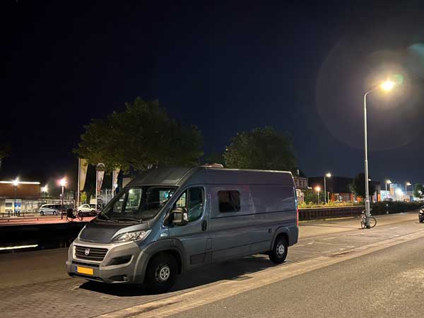 donkerblauwe camper in de nacht bij verlichte omgeving